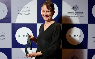 Professor Jane Pirkis holding research excellence award in front of NHMRC background