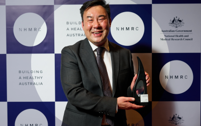 Professor Roger Chung holding research excellence award in front of NHMRC background