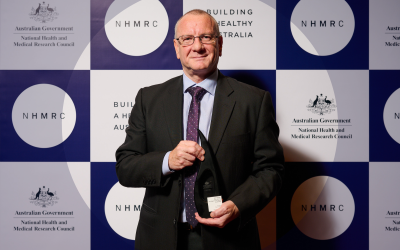 Professor Patrick Sexton holding research excellence award in front of NHMRC background